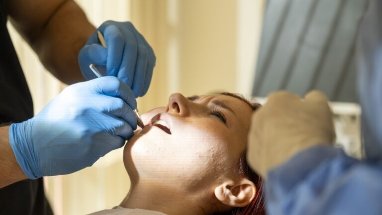 Close up image of a dentist placing a surgical dental implant into a patient's jawbone. The dentist is wearing surgical gloves and a mask. The image highlights the precision and care involved in the procedure.